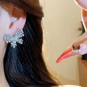 Detailansicht eines glitzernden Zirkon-Schmetterlingsohrrings mit Perlen am Ohr getragen.