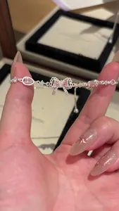 Detail view of a dainty silver bracelet featuring a pink zircon bow pendant.