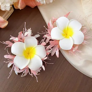 Detailansicht von zwei eleganten Frangipani Stoffblumen Haarklammern mit rosa Federakzenten.