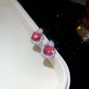 Close-up macro view of square red zircon stud earrings with sparkling halo and silver plating
