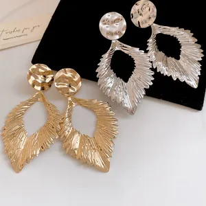 Close-up of elegant gold and silver metal ruffled leaf earrings on black velvet