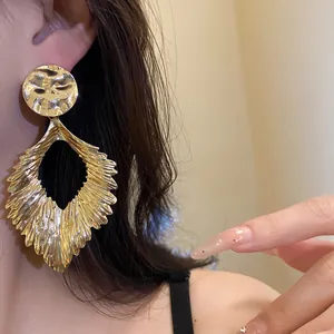Detailed view of large golden pleated leaf earrings with hammered texture on ear