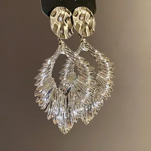 Macro detail view of silver metallic wrinkled leaf drop earrings with hammered texture