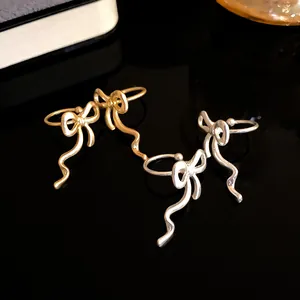 Close-up of matte gold and silver bowknot ear cuffs on a reflective black surface