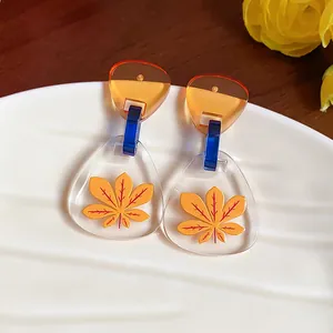 Primer plano de pendientes geométricos de acetato con estampado de hoja amarilla sobre resina