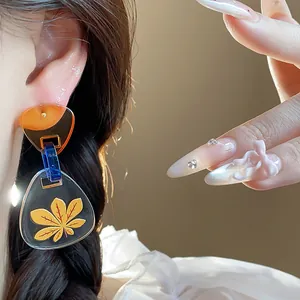 Primer plano de pendientes triangulares de acetato con estampado de hojas y detalle azul.