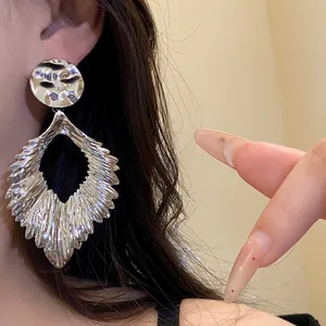 Detail shot of silver pleated leaf-shaped earrings on model ear showing large scale