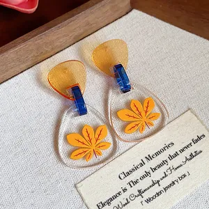 Primer plano detallado de pendientes de acetato con estampado de hojas amarillas