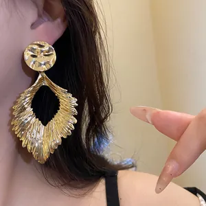 Detailed view of large golden leaf-shaped earrings featuring a hammered metal texture