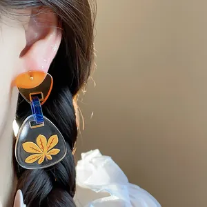 Detalle de pendientes triangulares de acetato con estampado de hoja amarilla