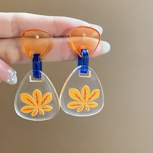 Vista detallada de pendientes de acetato con un diseño de estampado de hoja amarilla.