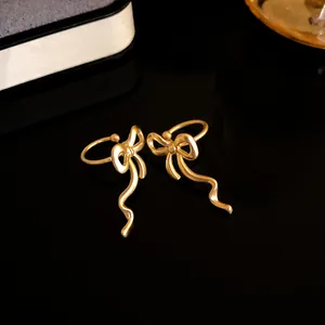 Close-up of elegant gold-toned bow-shaped ear cuffs on a dark reflective surface