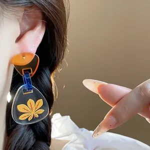 Vista detallada de aretes triangulares de acetato con estampado de hoja amarilla