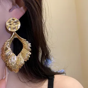 Detailed view of stylish gold pleated leaf drop earrings being worn to show scale and texture