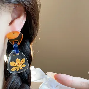 Primer plano de pendientes de acetato triangulares con diseño de hoja amarilla en modelo