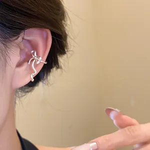 Close-up detail of an elegant silver bow-knot ear cuff worn on a person's ear cartilage.