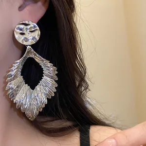 Detailed close-up of large silver wrinkled metal leaf earrings worn by a model