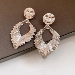 Macro view of silver-tone pleated leaf pendant earrings featuring a hammered metal texture