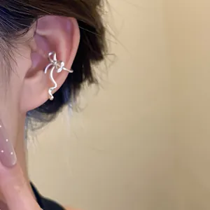 Close-up view of a delicate silver bowknot ear cuff clip worn on model's cartilage area