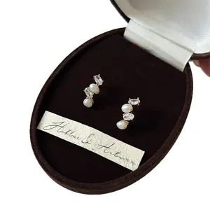 French style zircon and oval pearl stud earrings displayed in a luxury brown box