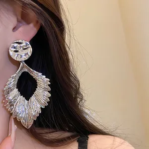 Detailed macro view showing the textured silver metallic pleated leaf pendant earrings worn on ear