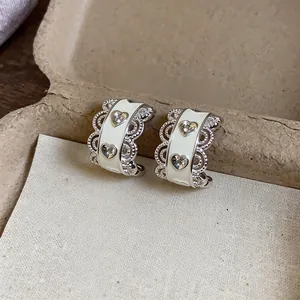 Close-up view of heart-shaped silver hoop earrings with white enamel and zircon accents
