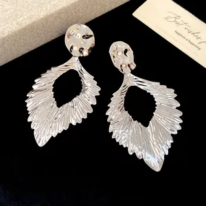 Close-up of metallic wrinkled leaf dangle earrings with a shiny silver finish.