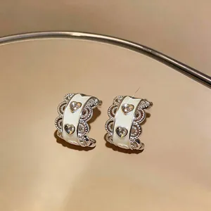 Close-up of elegant silver-tone hoop earrings with white enamel and heart zirconia