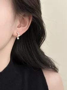Close-up of elegant pearl and zircon stud earrings worn on a model's ear for detail view.