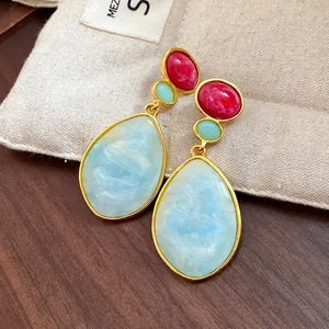 Macro detail of vintage teardrop earrings featuring vibrant red and sky blue resin stones.