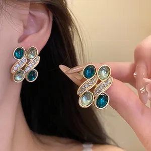 Close-up of vintage gold earrings with teal resin and rhinestones shown on ear and hand