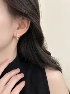 Close-up of elegant gold stud earrings featuring oval zircons and pearls on ear