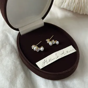 Close-up of French style pearl and zircon stud earrings in a brown velvet gift box.