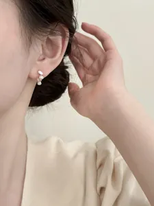 Close-up of elegant oval pearl and zircon stud earrings on model's ear for French style.