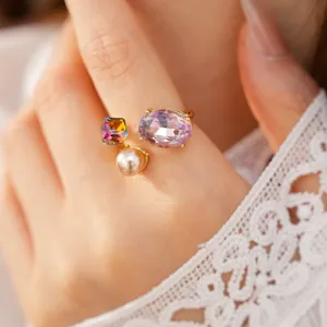 Close-up of an elegant gold adjustable ring featuring a purple crystal and white pearl.
