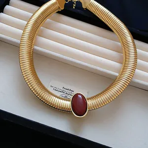 Gros plan sur un collier ras-de-cou doré de style vintage avec une pierre en résine rouge.