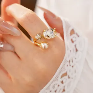 Detail view of an elegant gold open ring with oval stone and pearl on finger.