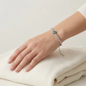 Close-up of an elegant silver-toned bracelet with a blue heart-shaped zircon worn on the wrist.