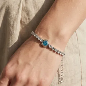 Detail of a sparkling tennis bracelet with a central blue heart-shaped gemstone on wrist