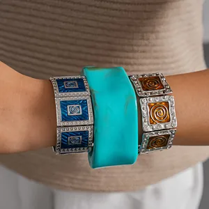 Close-up of vintage enamel square bracelets and wide turquoise resin bangle on wrist.