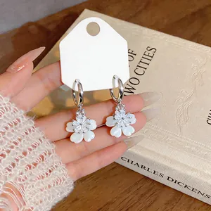 Macro view of exquisite white zircon flower hoop earrings held against a vintage book.
