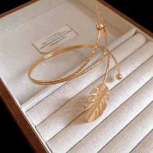 Detailed view of a golden metal spiral arm cuff featuring a delicate Monstera leaf motif.