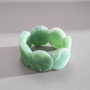 Détail d'un bracelet en acrylique marbré vert avec des pièces rondes géométriques liées.