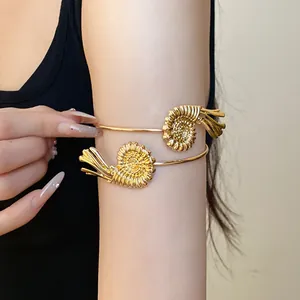 Detailed view of a gold-toned spiral shell arm cuff worn on a woman's upper arm.