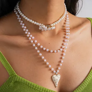 Dettaglio di collane di perle multistrato con ciondolo a cuore borchiato e fiore.