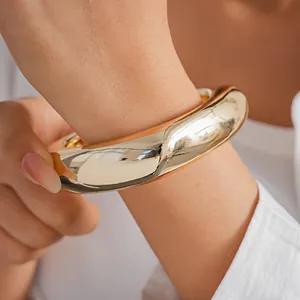 Gros plan d'un bracelet jonc épais en acrylique doré porté au poignet d'une femme.