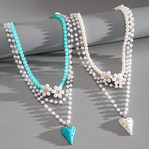 Primo piano di collane di perle a strati con fiori di strass e ciondoli a cuore.