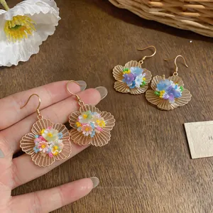 Vue détaillée de boucles d'oreilles fleurs ajourées dorées avec perles multicolores.