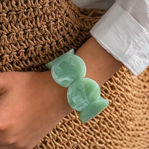 Gros plan d'un élégant bracelet géométrique en acrylique marbré vert sur un poignet féminin
