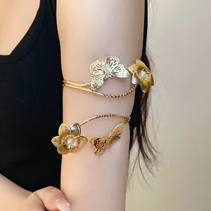 Macro detail of elegant gold metal arm cuff featuring delicate butterfly and floral pearl motifs